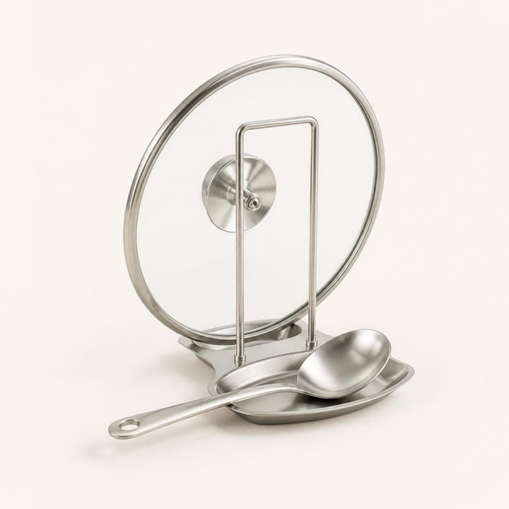 Stainless steel pot lid and spatula rack holding a glass lid and spoon, ivory background