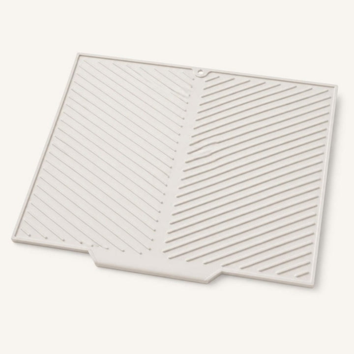 Light gray sloped silicone dish drying mat with diagonal ridges, ivory background