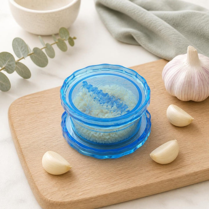 Blue garlic crusher with minced garlic on an oak cutting board with garlic cloves
