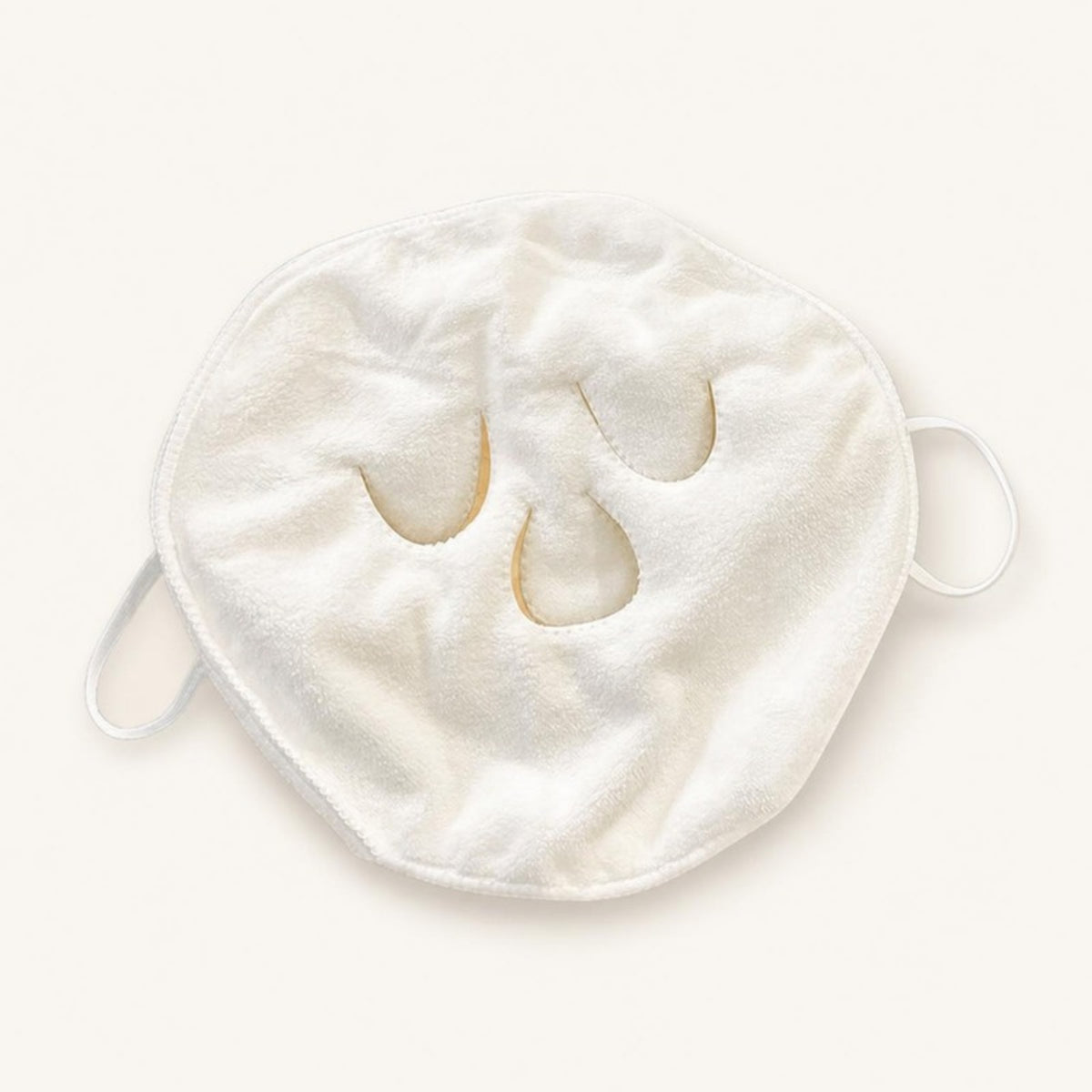 White three-hole compress face towel with ear loops lying flat on an ivory background