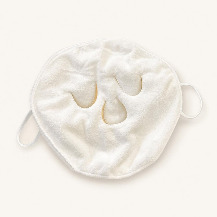 White three-hole compress face towel with ear loops lying flat on an ivory background