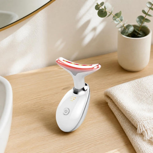 White LED neck and face device standing on a light oak bathroom vanity beside a linen towel and eucalyptus