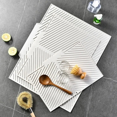 Stacked light gray silicone drying mats with a wooden spoon and brush, top view