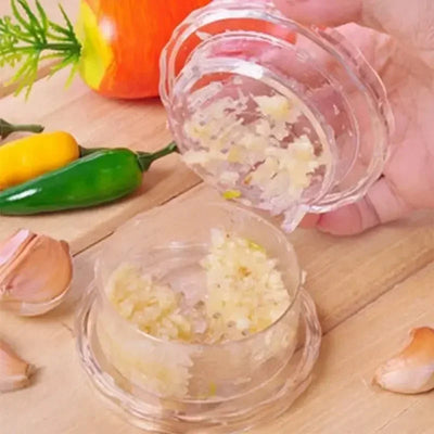 Clear garlic crusher filled with minced garlic on a wooden board