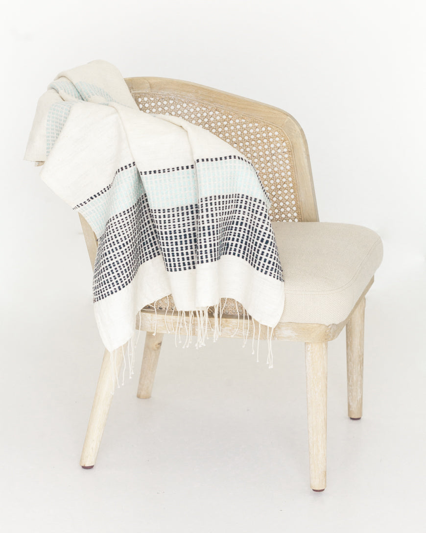 Camden handwoven cotton throw in Azure and Navy draped over a rattan-back chair