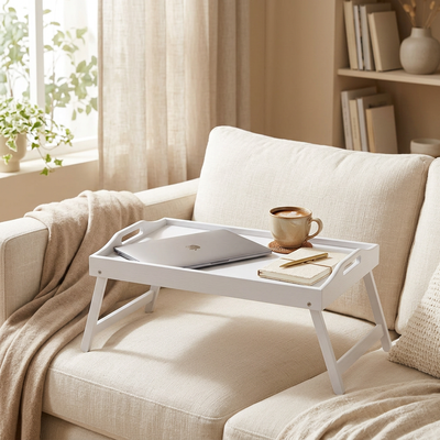 White foldable bamboo breakfast tray styled on a sofa with a laptop, coffee, and notebook